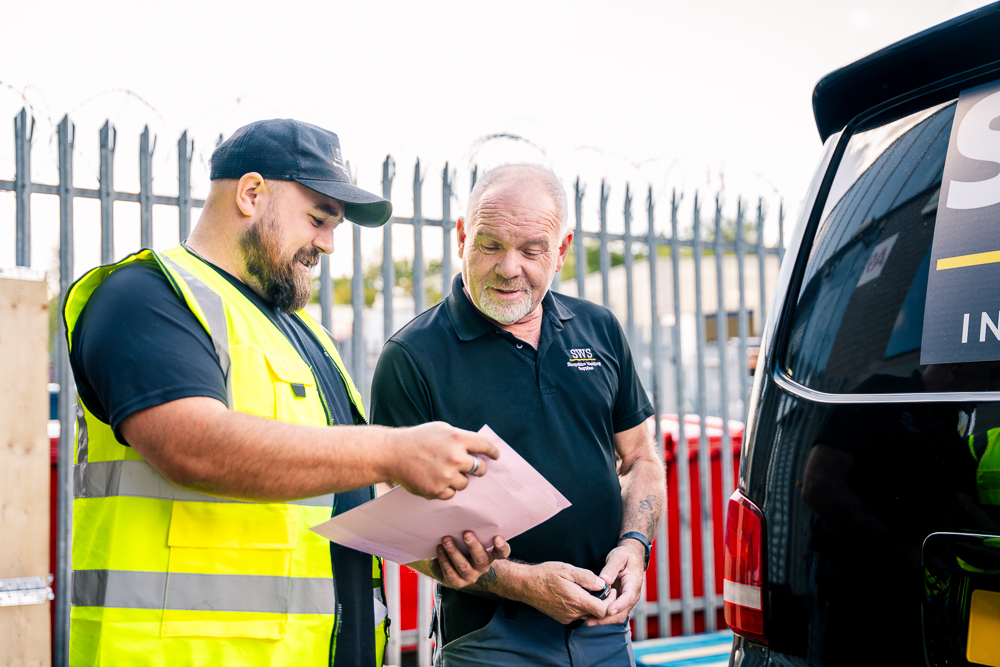 Technician discussing paperwork with a customer beside a vehicle.