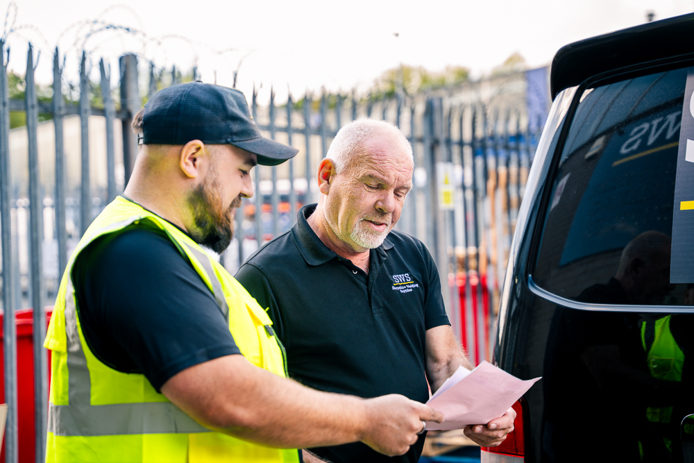 Warehouse worker handing a document to a customer beside a vehicle