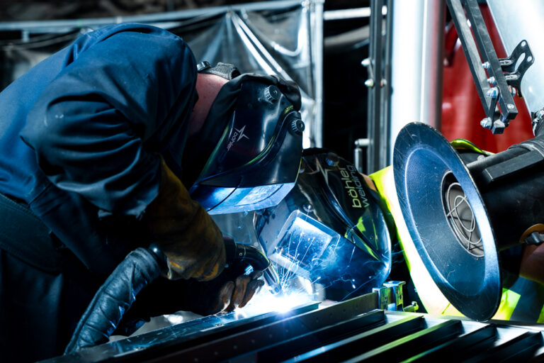 Welding technician using protective gear to weld metal components.