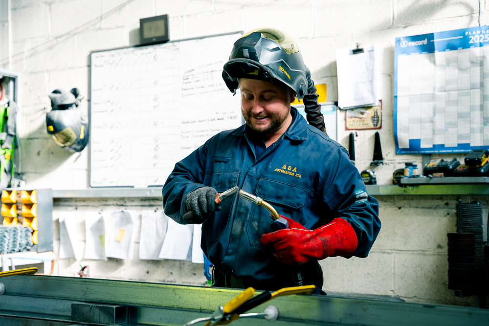 Welder holding welding torch and wearing protective helmet.