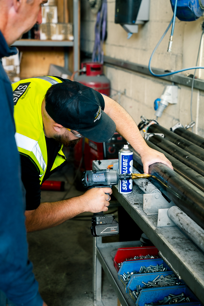 Technician drilling metal pipe in a workshop.