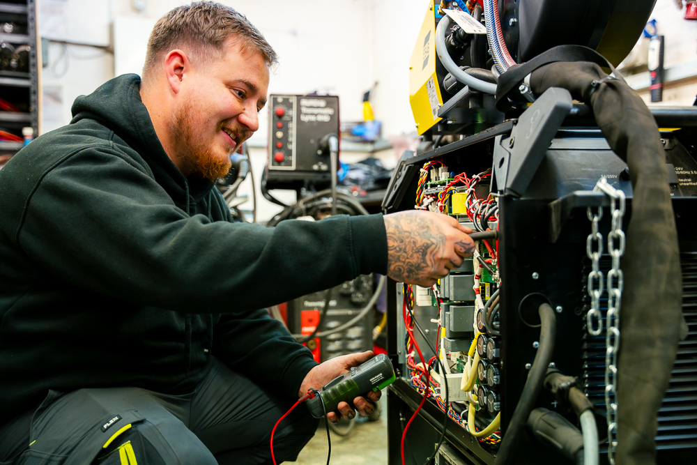 Technician wiring and testing electrical equipment in a workshop.
