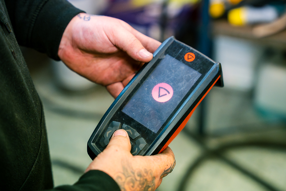 Shropshire Welding Solutions hand holding a digital control device in the workshop.
