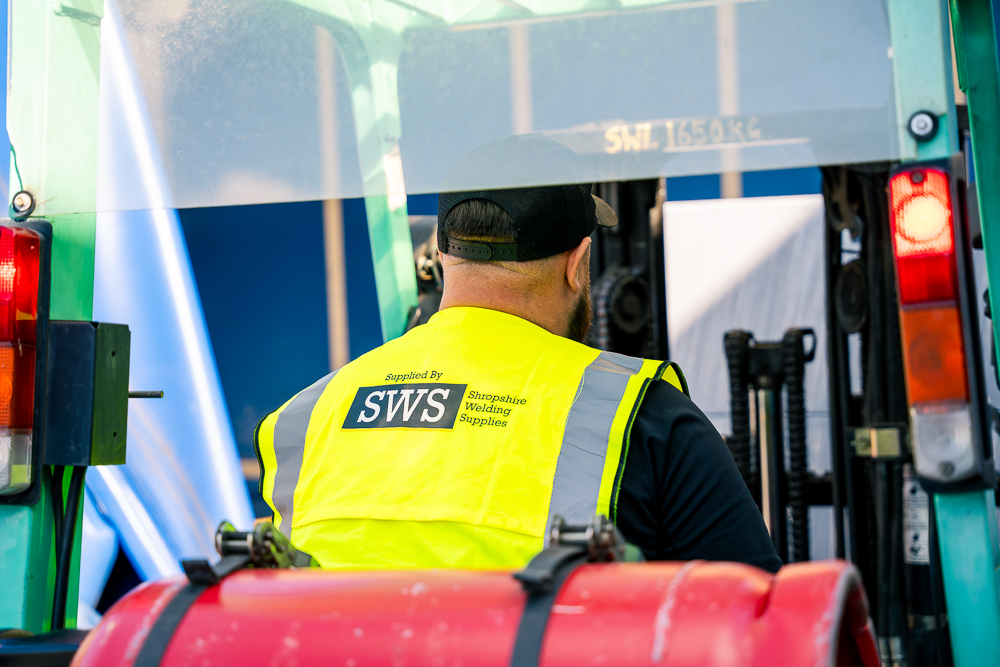 Worker in SWS vest driving machinery in workshop.